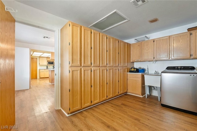 kitchen with sink, stainless steel microwave, washer / dryer, light brown cabinetry, and light wood-type flooring