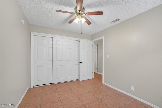 unfurnished bedroom with ceiling fan, a closet, light tile patterned flooring, and a textured ceiling