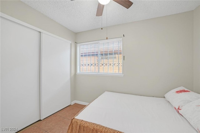 bedroom with light tile patterned floors, a textured ceiling, a closet, and ceiling fan