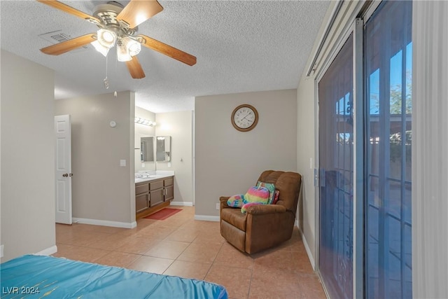 tiled bedroom featuring ceiling fan, sink, ensuite bathroom, and a textured ceiling