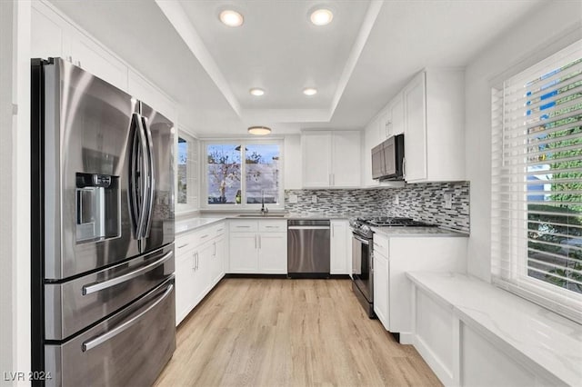 kitchen with a tray ceiling, white cabinetry, light wood-type flooring, and appliances with stainless steel finishes