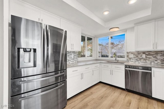 kitchen featuring appliances with stainless steel finishes, light wood-type flooring, a raised ceiling, sink, and white cabinets