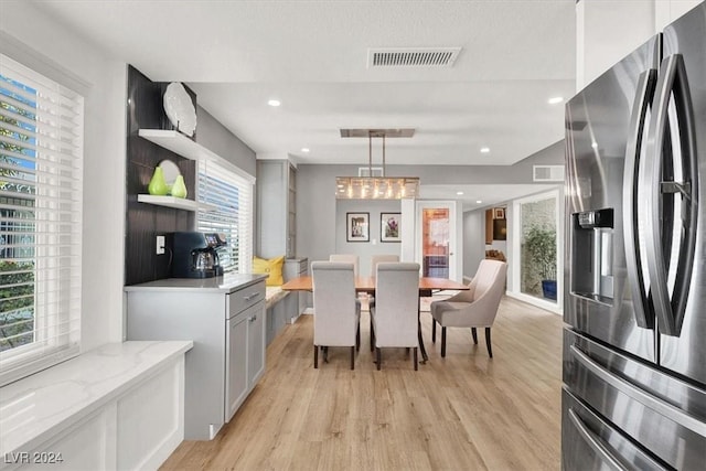 kitchen with decorative light fixtures, stainless steel fridge, light stone counters, and light hardwood / wood-style floors