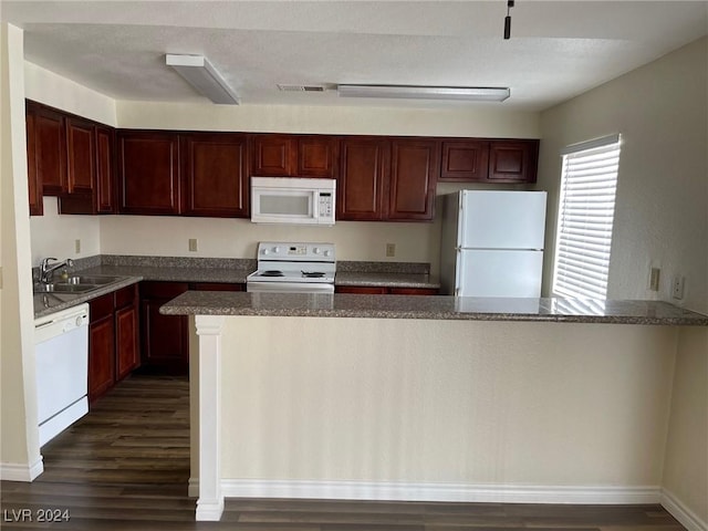 kitchen with kitchen peninsula, white appliances, sink, dark stone countertops, and dark hardwood / wood-style floors