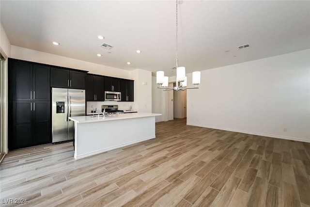 kitchen with appliances with stainless steel finishes, decorative light fixtures, a chandelier, light hardwood / wood-style floors, and an island with sink