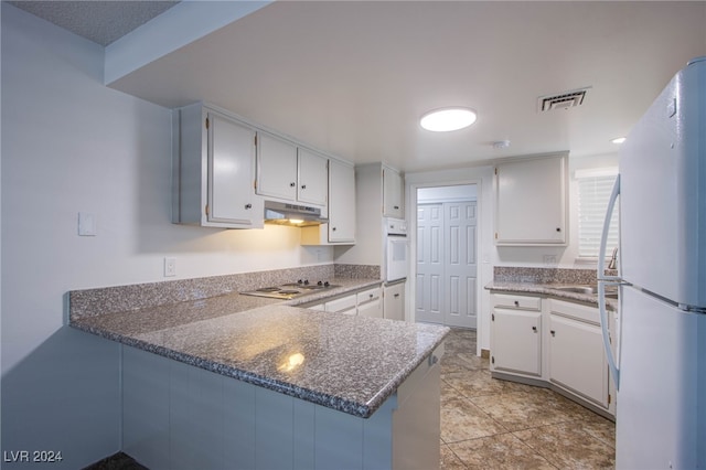 kitchen with kitchen peninsula, white cabinetry, dark stone counters, and white appliances