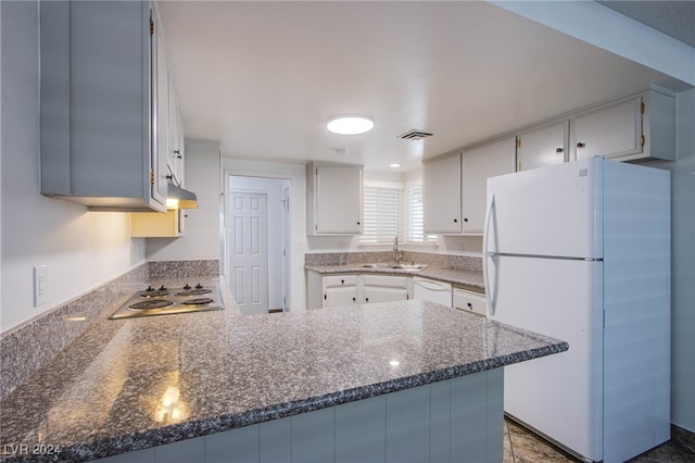 kitchen with kitchen peninsula, white appliances, dark stone countertops, and sink