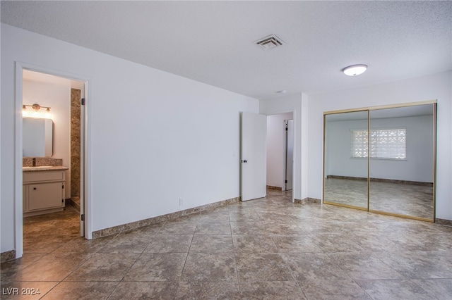 unfurnished bedroom with ensuite bath, a closet, a textured ceiling, and sink