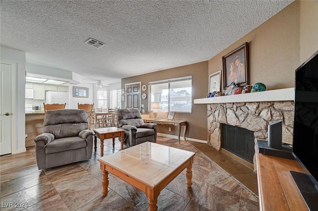 living room featuring a textured ceiling, a fireplace, and ceiling fan