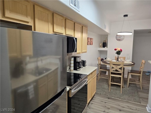 kitchen featuring light brown cabinets, stainless steel appliances, hanging light fixtures, and light hardwood / wood-style floors