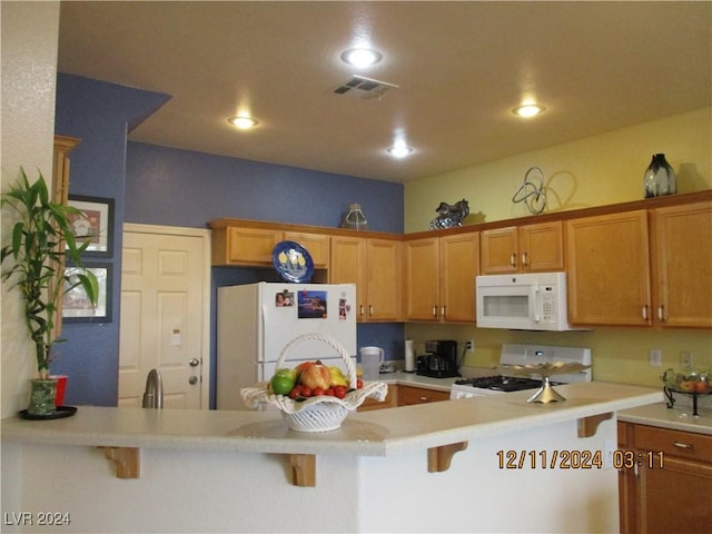 kitchen with a kitchen bar, white appliances, and kitchen peninsula