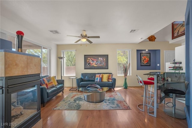 living area featuring visible vents, baseboards, ceiling fan, and wood finished floors