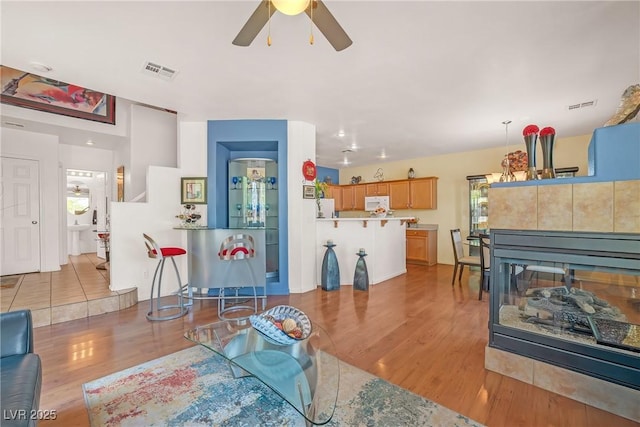 living area featuring ceiling fan, light wood finished floors, and visible vents