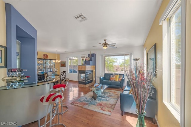 living area with a ceiling fan, visible vents, a tiled fireplace, and wood finished floors