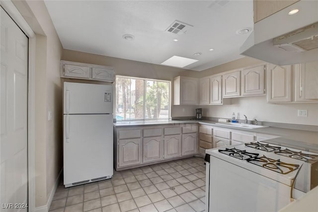 kitchen featuring white appliances, white cabinets, sink, a skylight, and light tile patterned floors