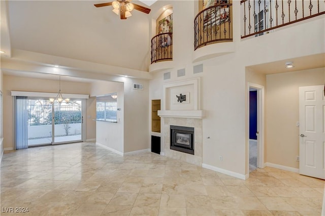 unfurnished living room featuring a tile fireplace, a high ceiling, and ceiling fan with notable chandelier