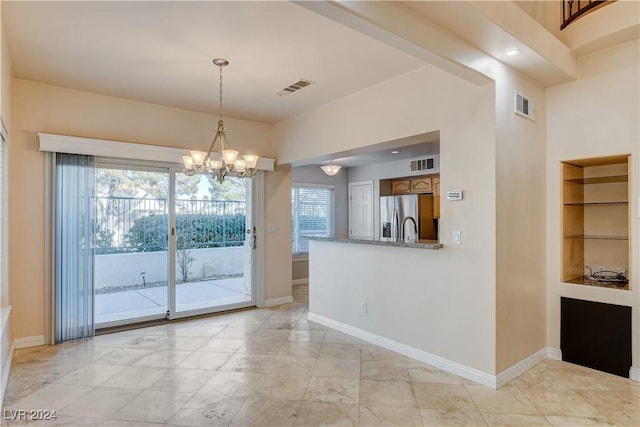 interior space featuring stainless steel refrigerator with ice dispenser, built in shelves, decorative light fixtures, light stone counters, and a chandelier