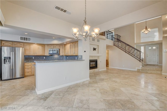 kitchen with backsplash, dark stone counters, stainless steel appliances, a tile fireplace, and decorative light fixtures