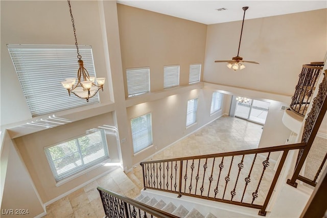 staircase featuring ceiling fan with notable chandelier and a towering ceiling