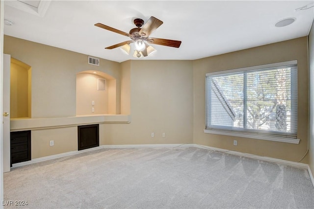 empty room with built in desk, light colored carpet, and ceiling fan