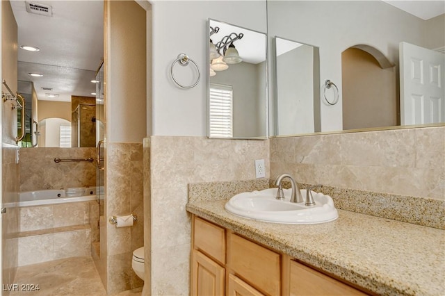 bathroom featuring tiled bath, vanity, tile walls, and toilet