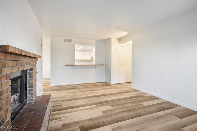 unfurnished living room featuring light wood-type flooring and a brick fireplace