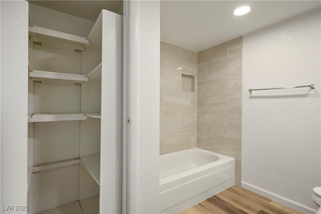 bathroom with tiled shower / bath combo, toilet, and wood-type flooring