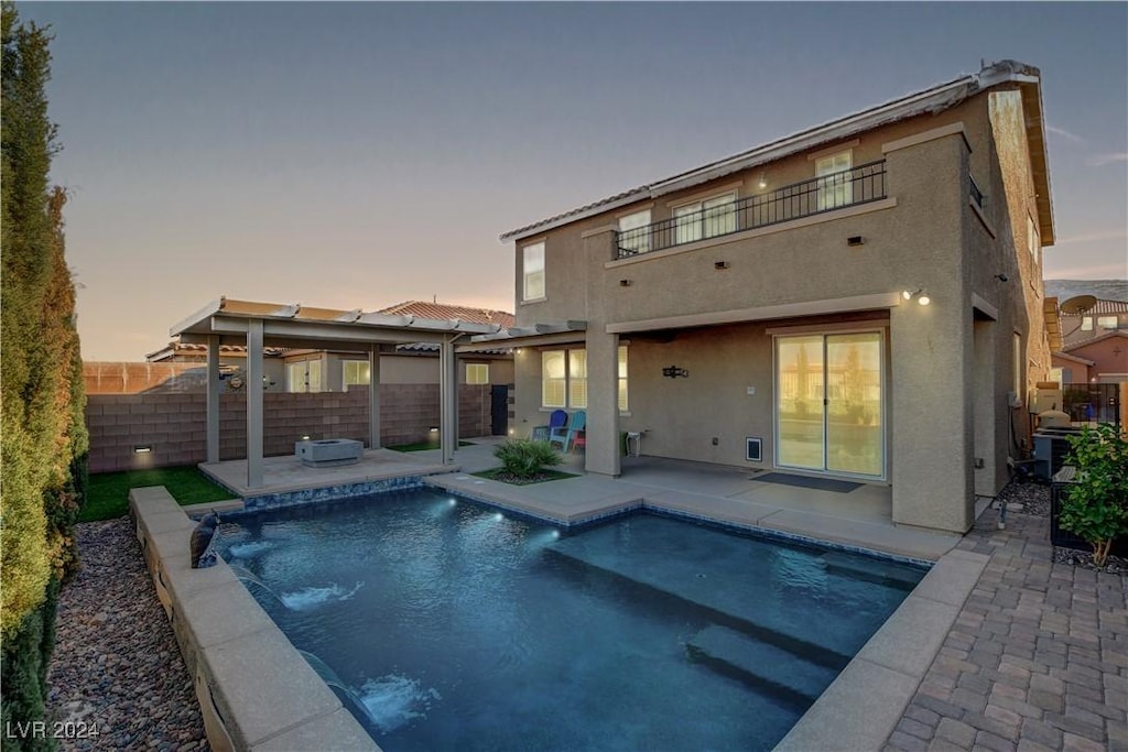 back house at dusk with a fenced in pool, pool water feature, a balcony, and a patio