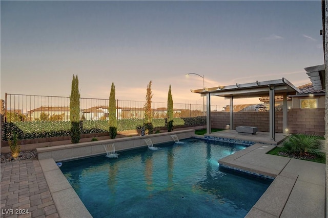 pool at dusk with pool water feature and a patio area