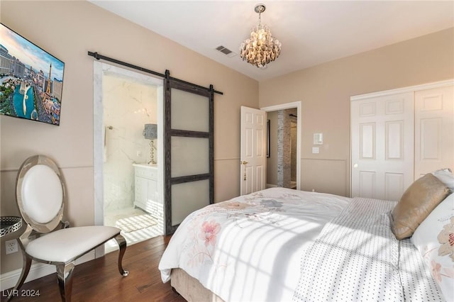 bedroom featuring a chandelier, a barn door, dark wood-type flooring, ensuite bath, and a closet