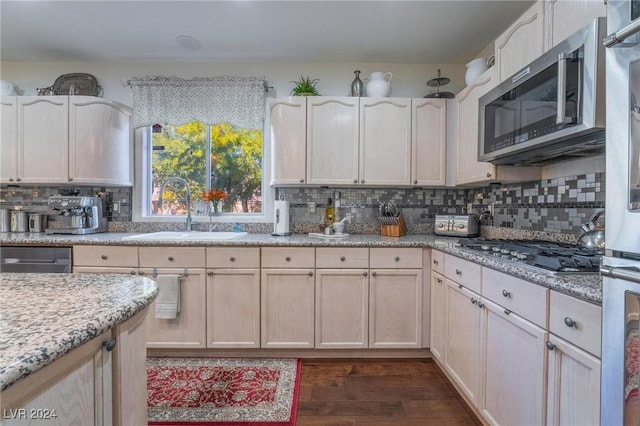 kitchen featuring sink, light stone counters, dark hardwood / wood-style floors, stainless steel appliances, and decorative backsplash