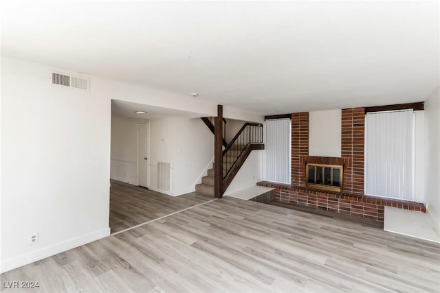 unfurnished living room with a brick fireplace and light hardwood / wood-style flooring