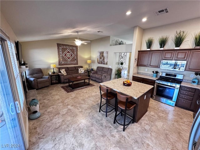 kitchen featuring ceiling fan, stainless steel range, vaulted ceiling, a breakfast bar, and a kitchen island