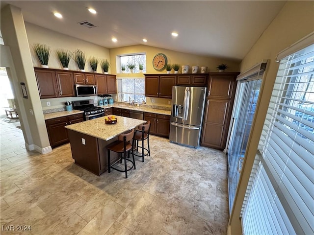 kitchen with appliances with stainless steel finishes, a kitchen breakfast bar, vaulted ceiling, sink, and a center island