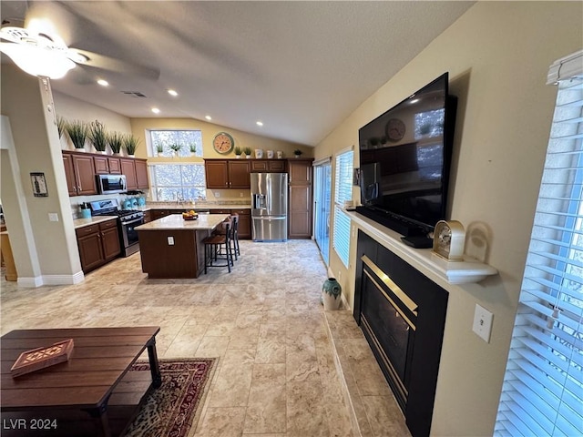 kitchen with appliances with stainless steel finishes, a breakfast bar, vaulted ceiling, ceiling fan, and a center island