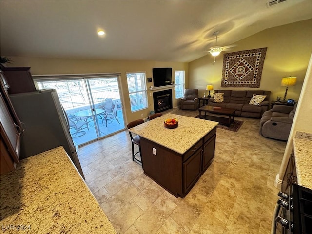 kitchen with light stone counters, dark brown cabinetry, ceiling fan, a center island, and lofted ceiling