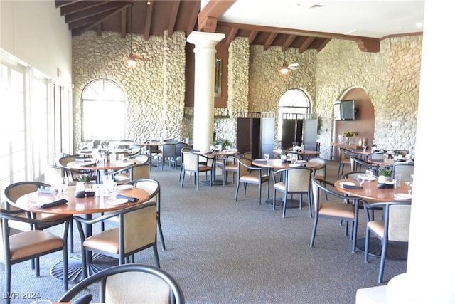 carpeted dining space with decorative columns, beamed ceiling, and high vaulted ceiling