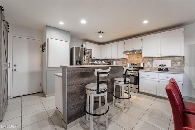 kitchen featuring a center island with sink, a kitchen breakfast bar, white cabinets, a barn door, and appliances with stainless steel finishes