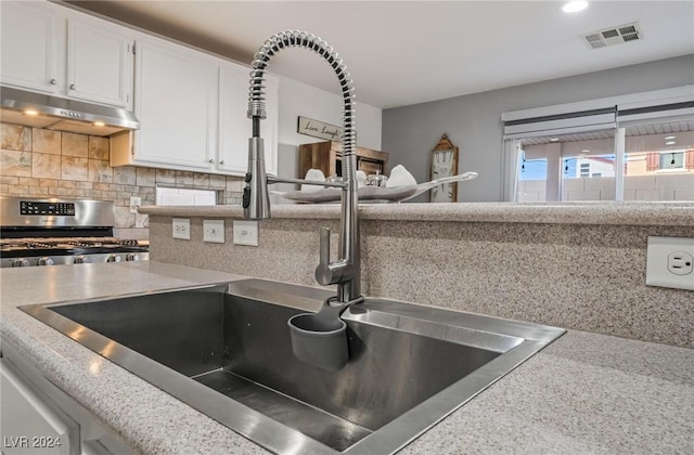 kitchen with stainless steel gas range oven, sink, white cabinetry, and backsplash