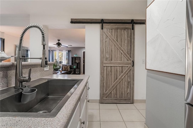 kitchen featuring white cabinets, sink, ceiling fan, a barn door, and light tile patterned floors