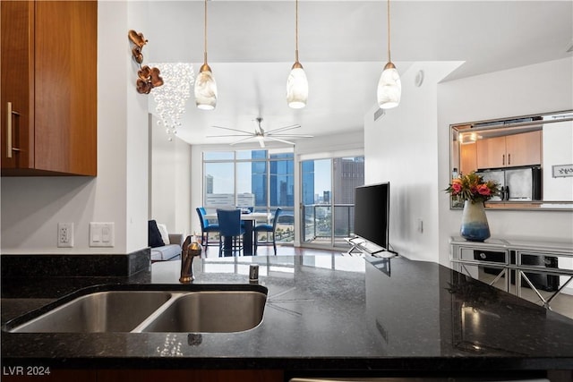 kitchen featuring floor to ceiling windows, dark stone counters, sink, hanging light fixtures, and ceiling fan