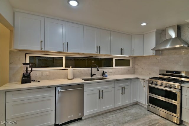 kitchen featuring sink, wall chimney range hood, decorative backsplash, white cabinets, and appliances with stainless steel finishes