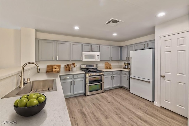 kitchen with visible vents, light wood-type flooring, gray cabinets, white appliances, and a sink