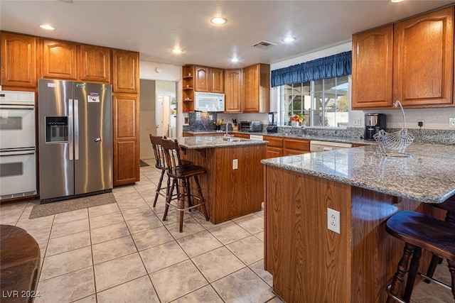 kitchen featuring white appliances, light stone countertops, light tile patterned floors, a kitchen island, and a breakfast bar area