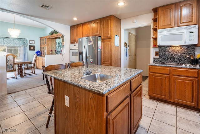 kitchen featuring white appliances, a kitchen island with sink, sink, a chandelier, and hanging light fixtures