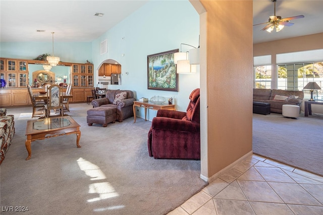 carpeted living room featuring a high ceiling and ceiling fan with notable chandelier