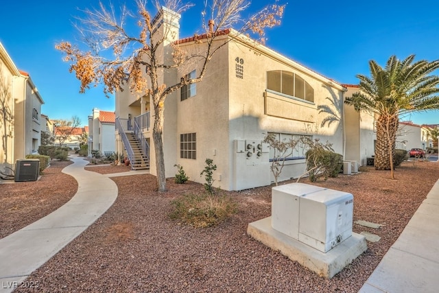 view of home's exterior featuring stairway, a chimney, cooling unit, and stucco siding