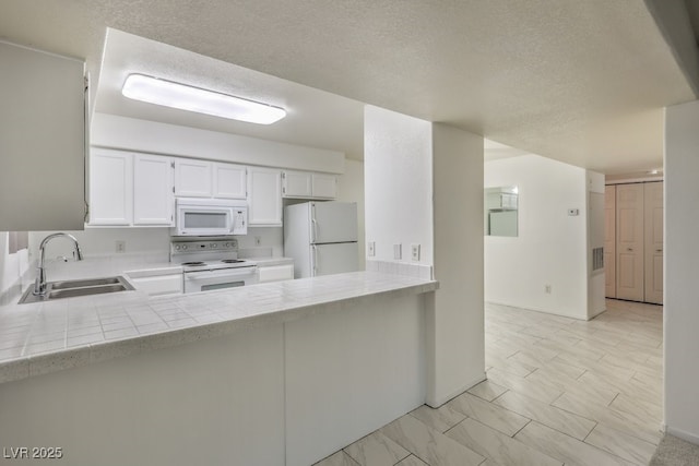 kitchen featuring white cabinets, a sink, a textured ceiling, white appliances, and a peninsula