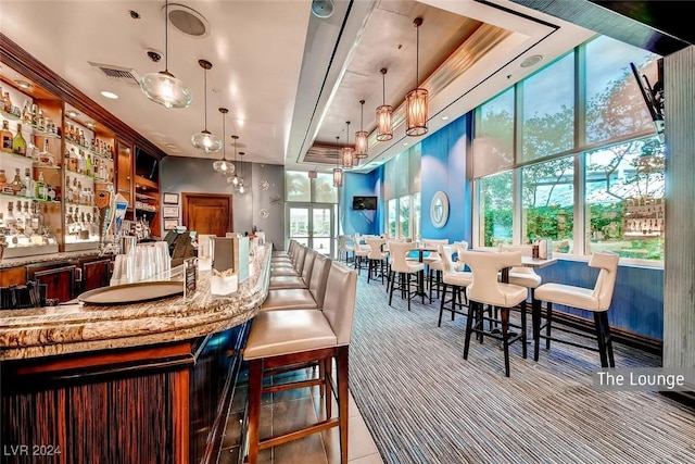 bar with light stone countertops, pendant lighting, a raised ceiling, and light tile patterned flooring