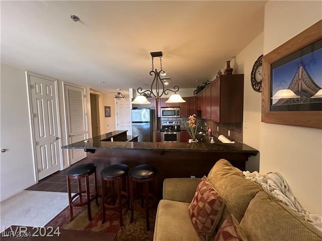 kitchen featuring kitchen peninsula, appliances with stainless steel finishes, tasteful backsplash, dark tile patterned flooring, and hanging light fixtures